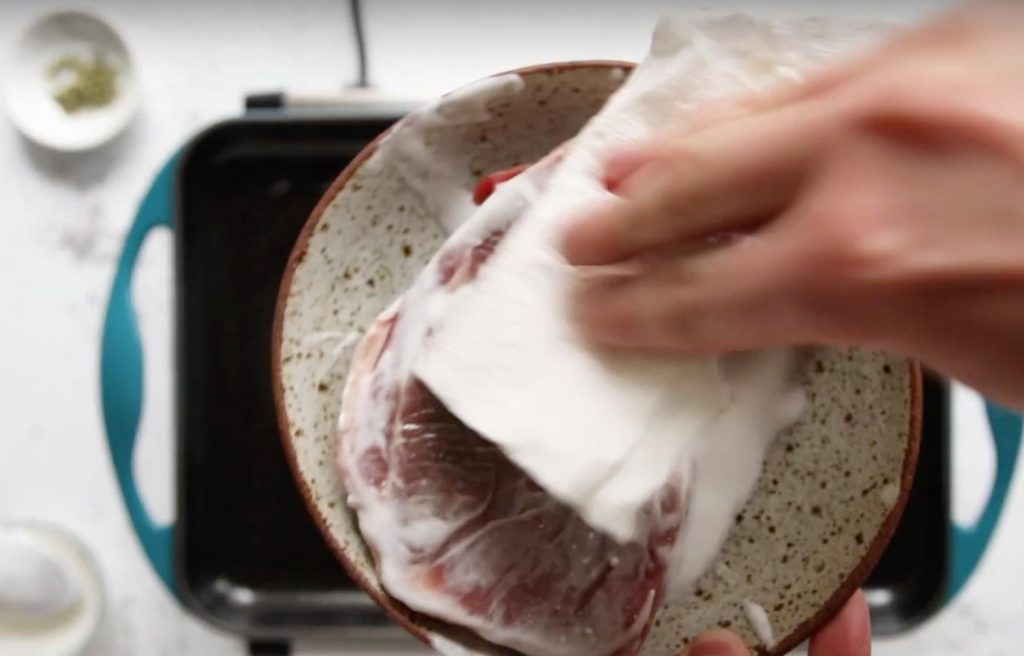 paper towel blotting yogurt off lamb on a plate