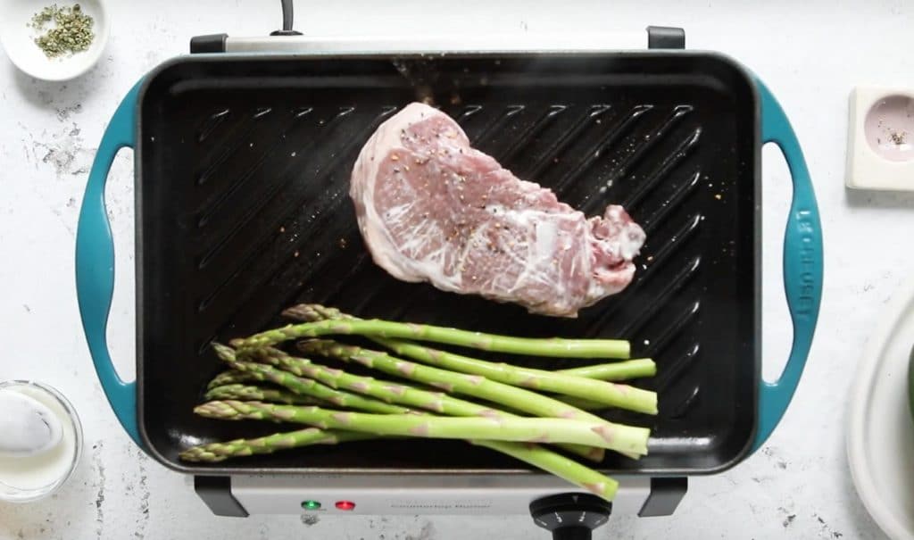lamb steak with yogurt on top and asparagus on grill pan