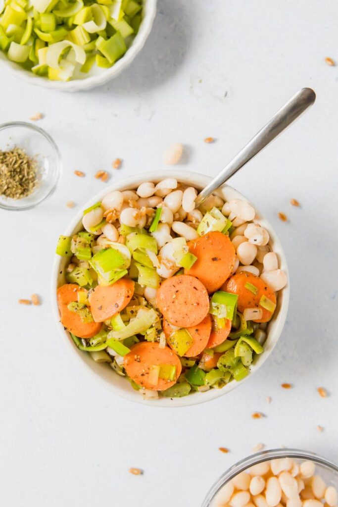 white bean and farro bowl with carrots and leeks in a bowl, with ingredients on table