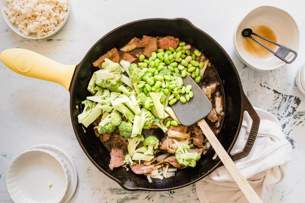 beef, broccoli, and edamame cooking in a cast iron skillet