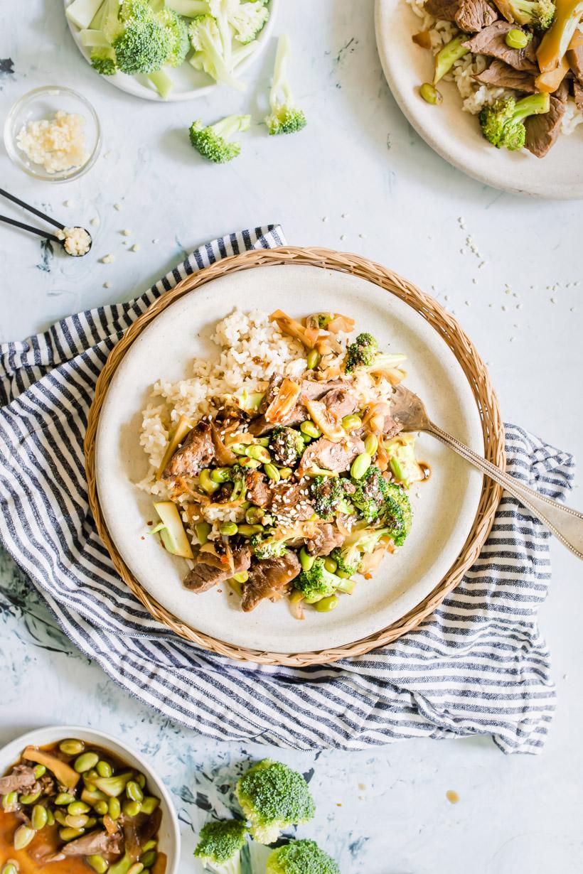 beef and broccoli over rice on a plate with ingredients surrounding it