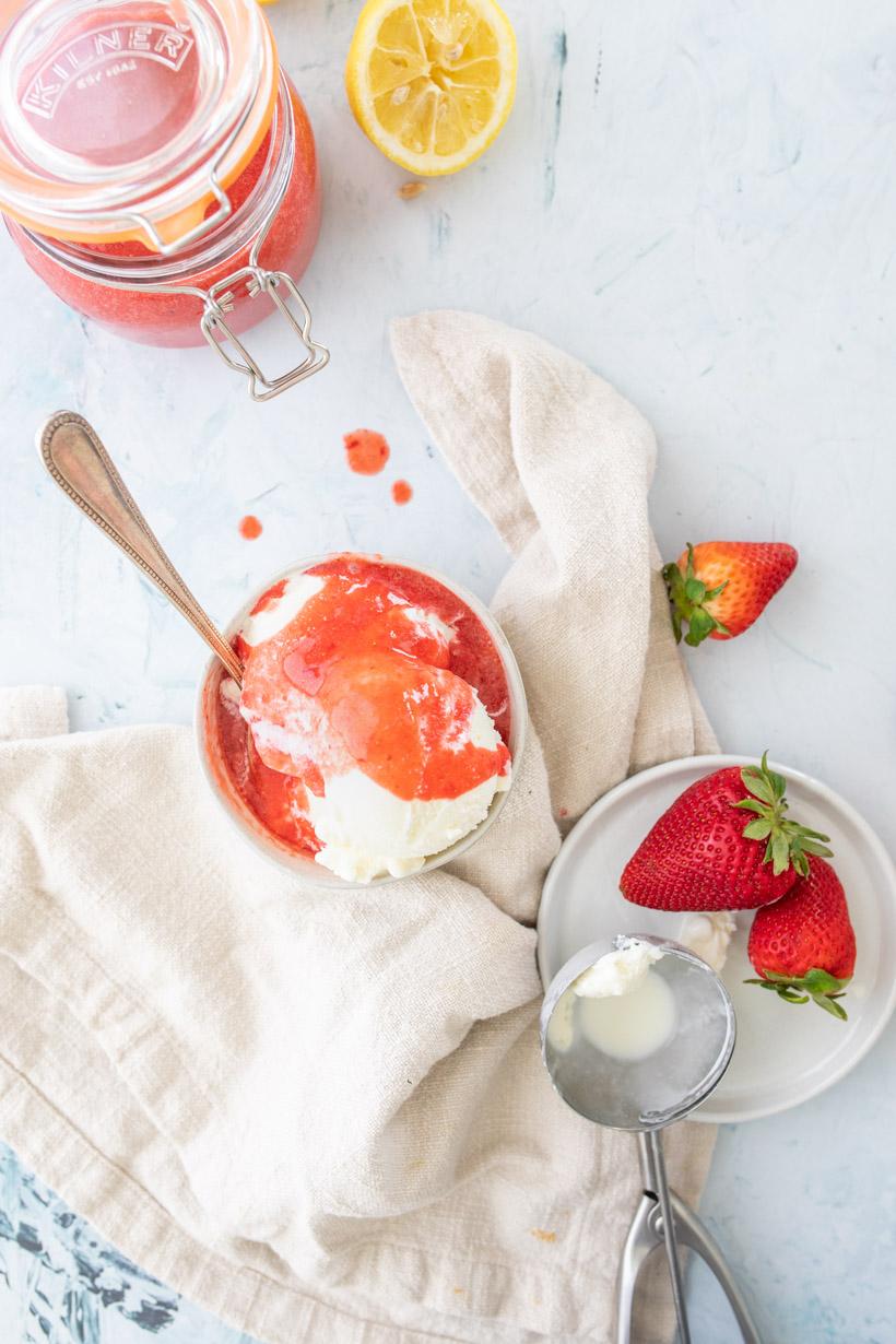 ice cream with strawberry sauce in a bowl with ingredients surrounding it
