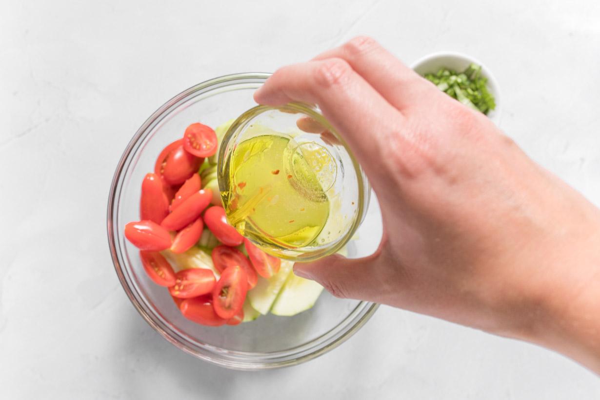 pouring vinaigrette onto sliced tomatoes and cucumbers