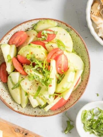 tomato and cucumber salad in bowl, with chicken and other ingredients around