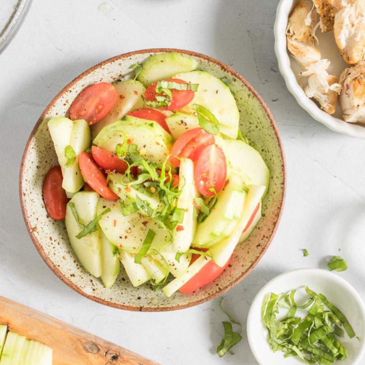 tomato and cucumber salad in bowl, with chicken and other ingredients around