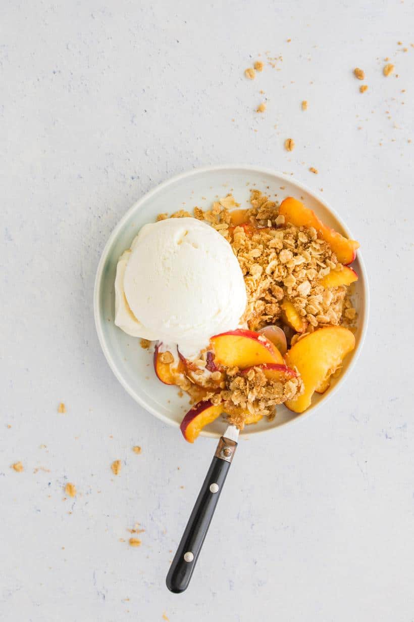 peach with crumble topping in a bowl with ice cream