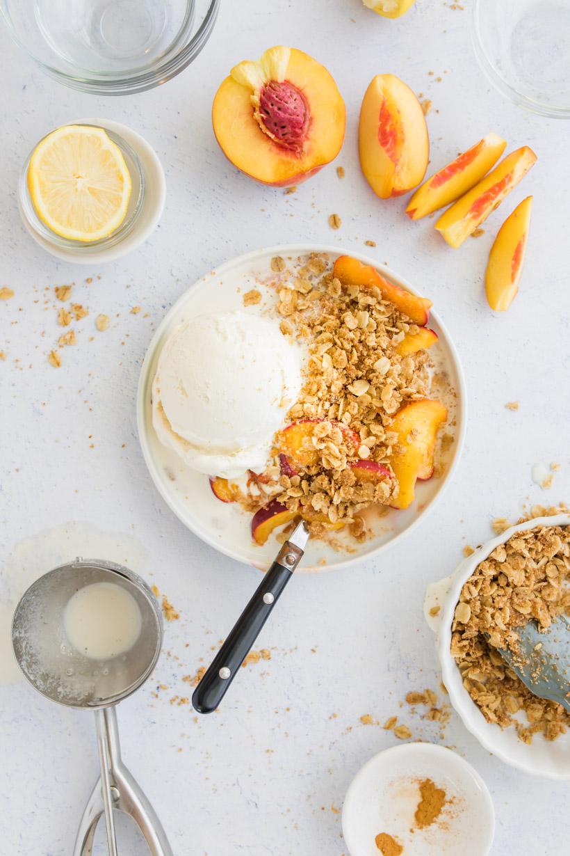 peach crumble in a bowl with ice cream and ingredients on a table