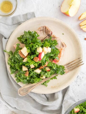 kale apple and pecan salad over a pork chop with ingredients on a table