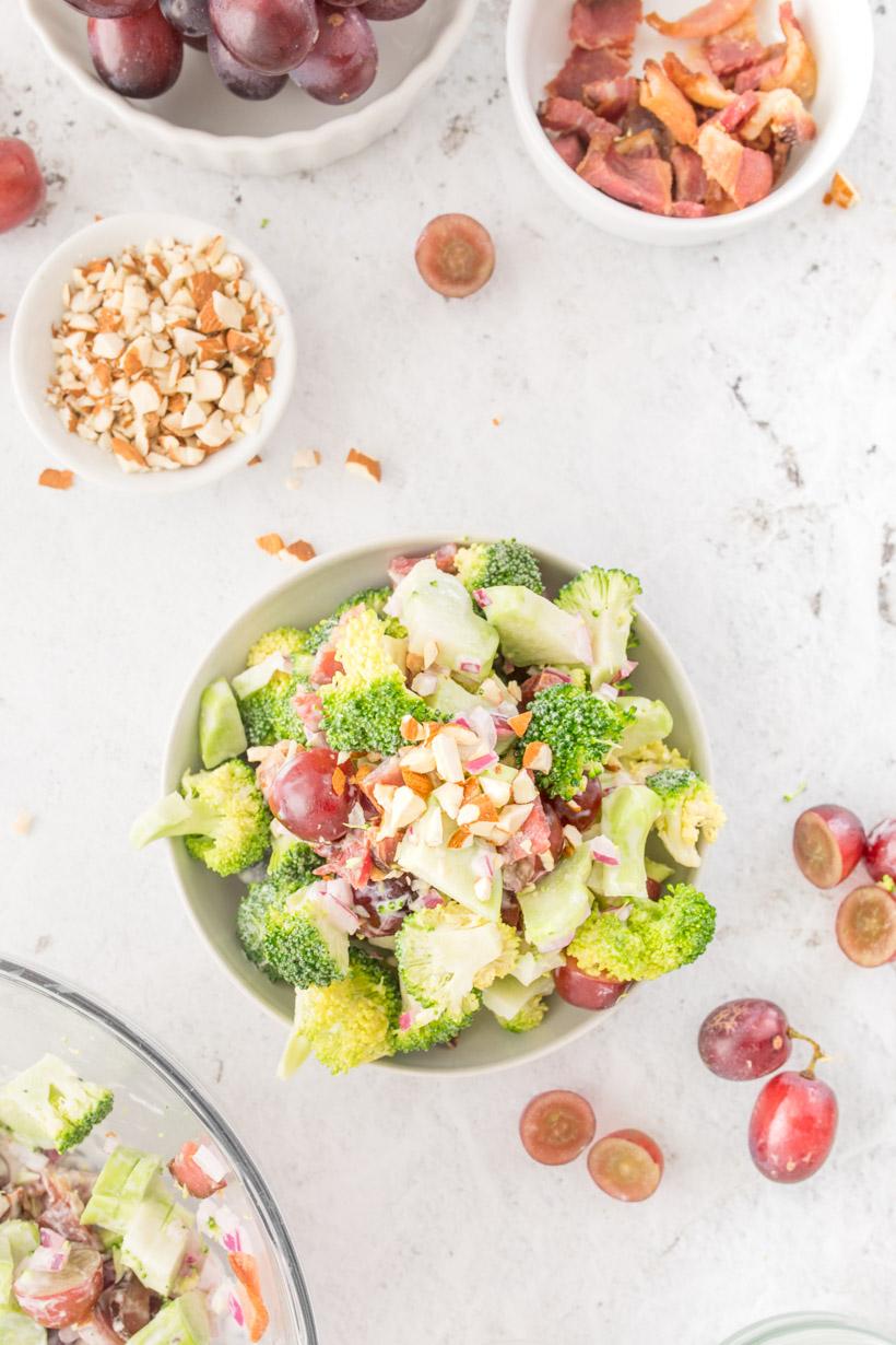 broccoli salad with grapes in a bowl with extra ingredients on the table