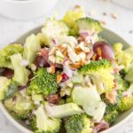 close up of broccoli salad with grapes in a bowl with ingredients in background
