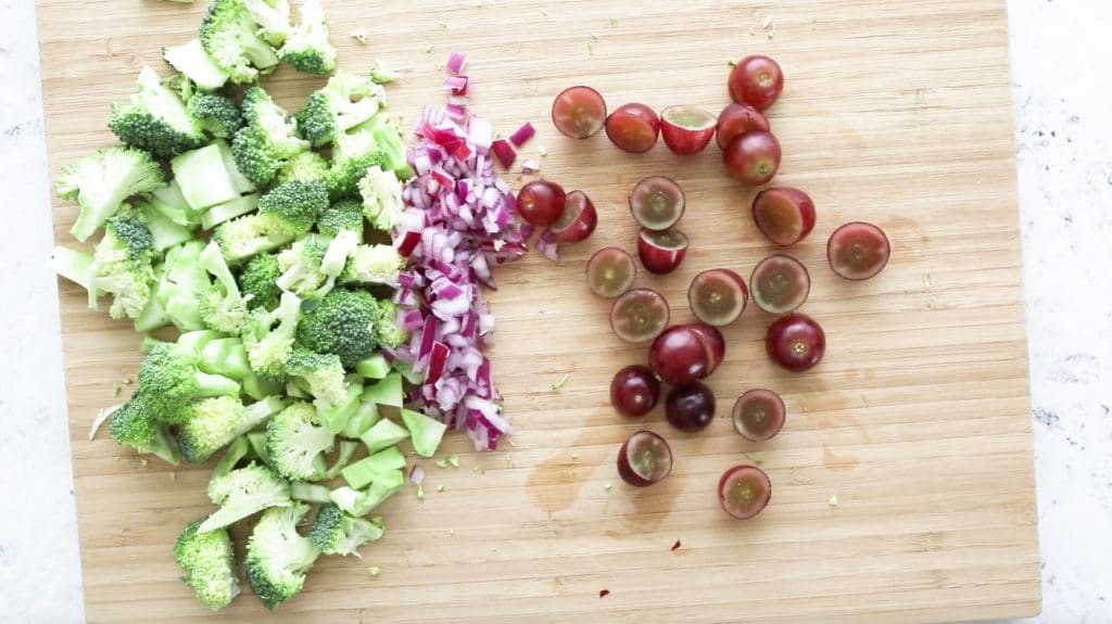 chopped broccoli, red onion, and grapes on a cutting board