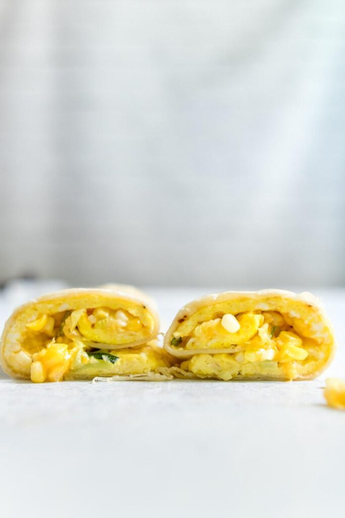 two halves of egg, vegetable, and cheese wrapped up in a tortilla