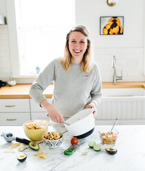 Rebecca of Nourish Nutrition Blog in a kitchen making guacamole with chips and dips on counter