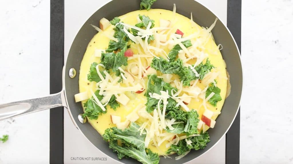 egg omelette in a pan with kale, apples, and cheese on top