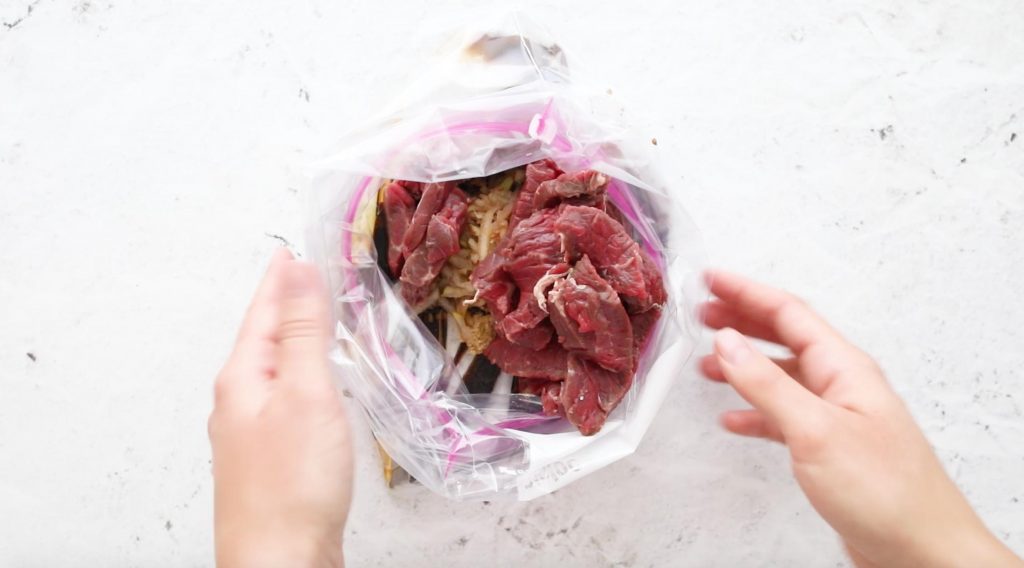hands holding a plastic bag full of beef with marinade ingredients in it