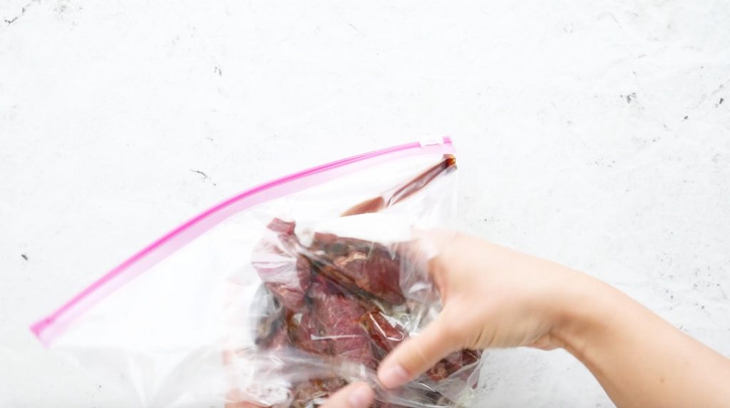 two hands holding marinating beef in a plastic bag