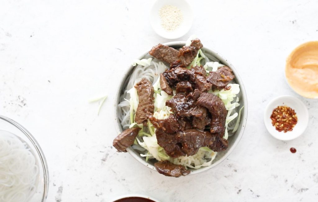 Korean bulgogi in a bowl with ingredients surrounding it