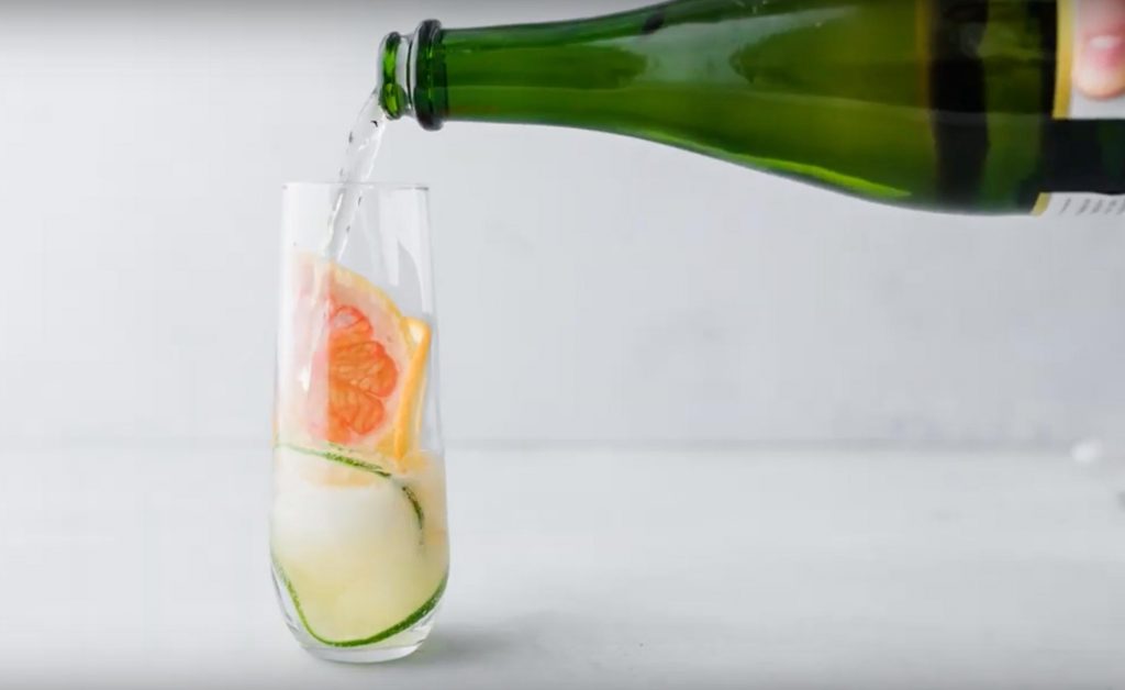 pouring apple cider into champagne glass with sliced citrus in it