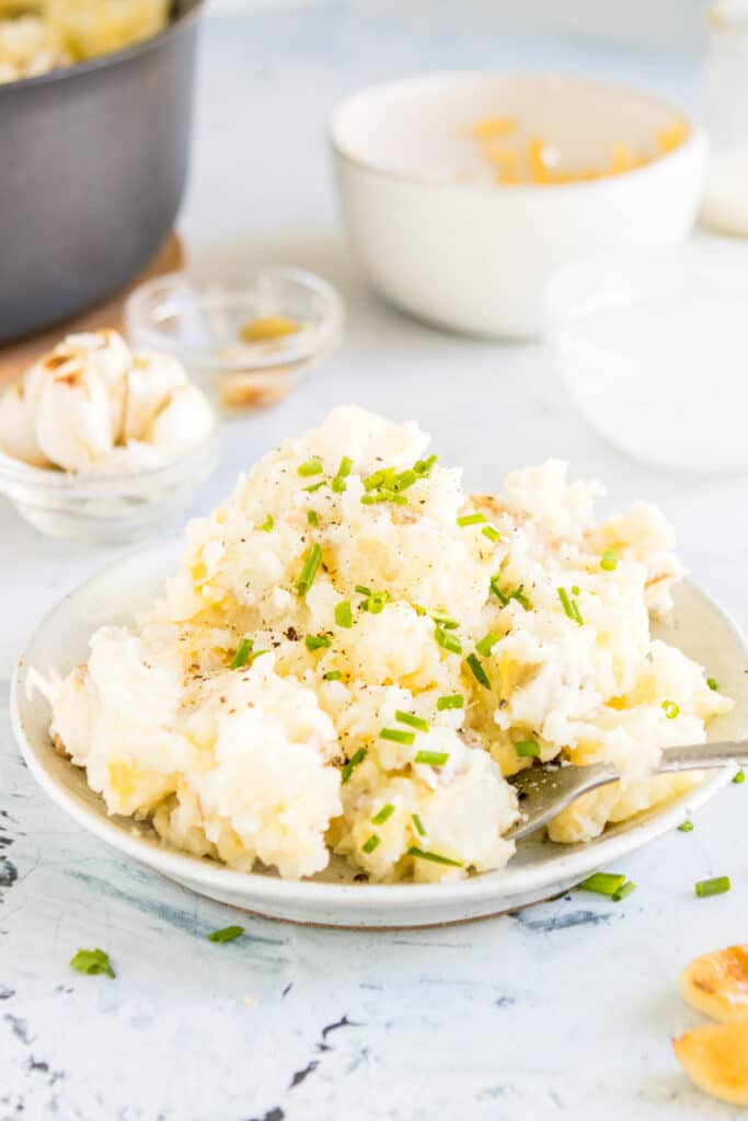 cheesy garlic mashed potatoes with chives on top and other ingredients behind them