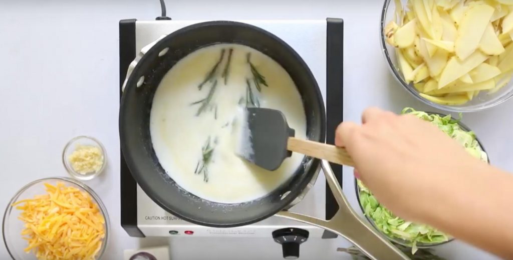 stirring two rosemary sprigs in a pot of milk