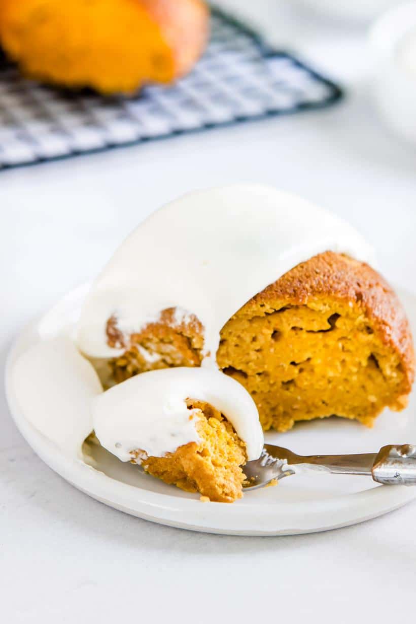 pumpkin cake with cream cheese whipped cream with a slice cut out on a plate