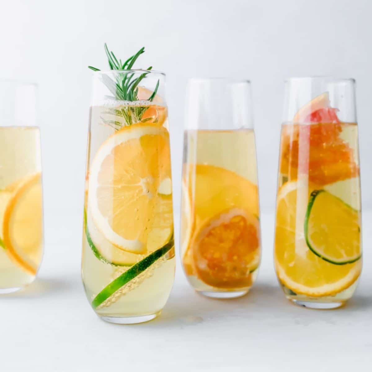 4 glasses of apple drink with citrus slices in it