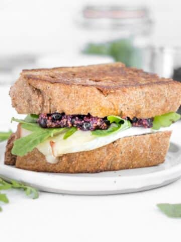 two slices of bread with cheese, arugula, and blueberry mustard between