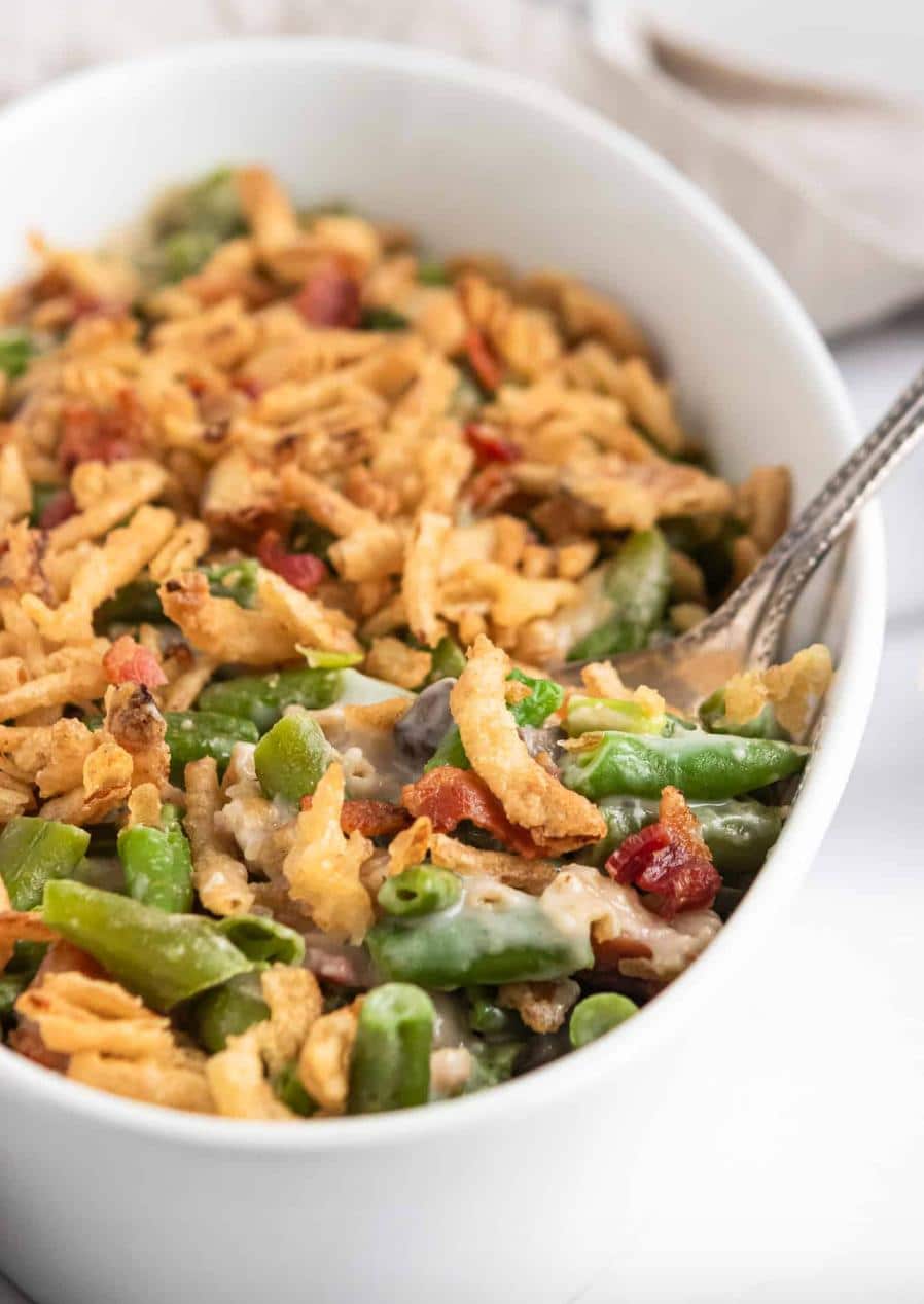 green bean casserole with bacon and fried onions in a white oval baking dish