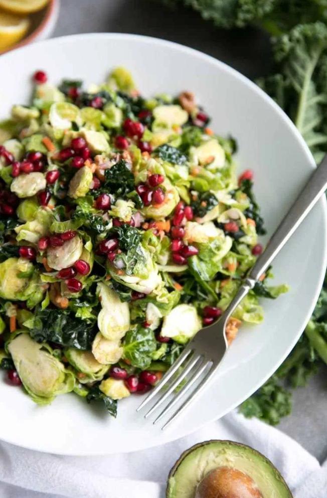 shredded brussels sprouts and kale salad with pomegranates on a plate with a fork