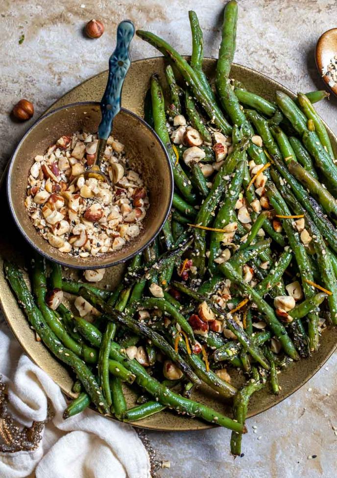 sauteed green beans with hazlenuts on top next to a bowl of chopped hazelnuts