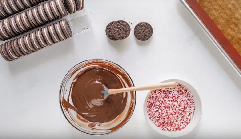 bowl of melted chocolate, crushed peppermint candies and oreos on a table