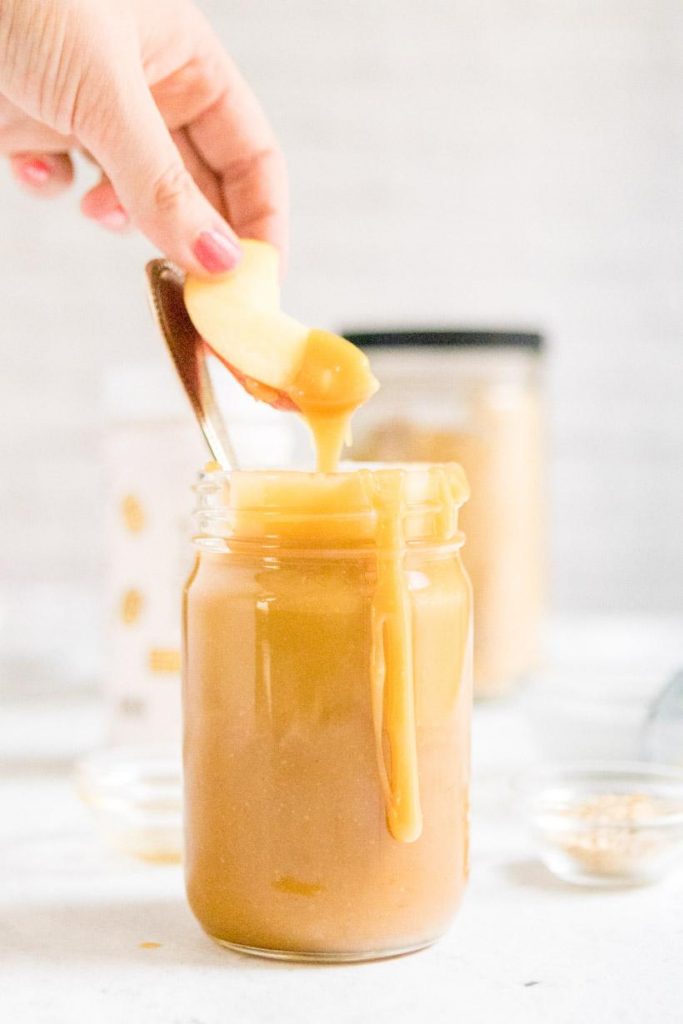 dipping apple into peanut butter caramel sauce in a jar