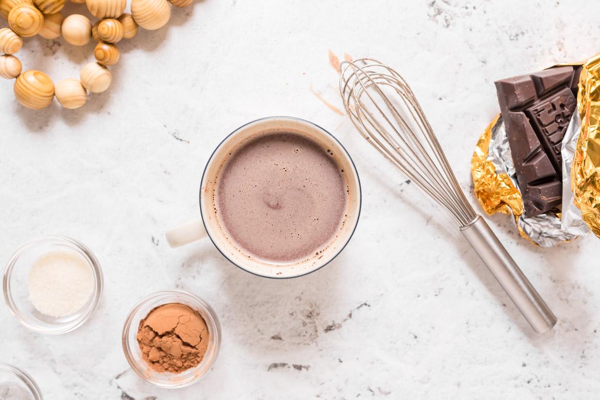 hot cocoa with whisk and other ingredients surrounding it on a table