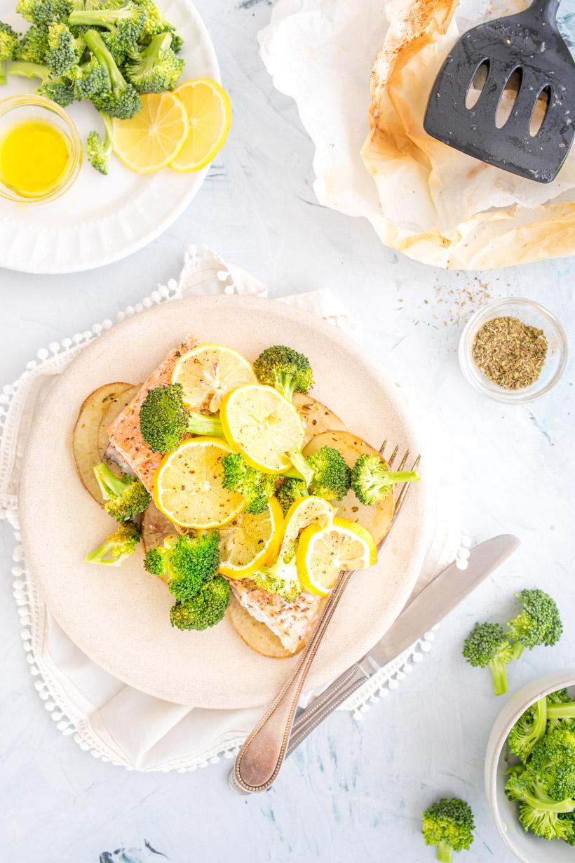 salmon in a bag made of parchment paper on a plate with other ingredients around it