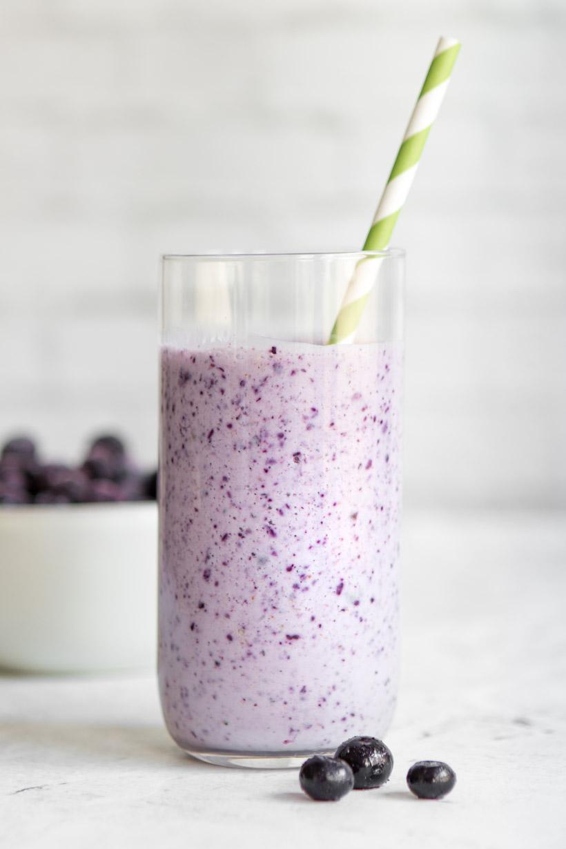 blueberry tea smoothie in a tall glass with green and white striped straw in it