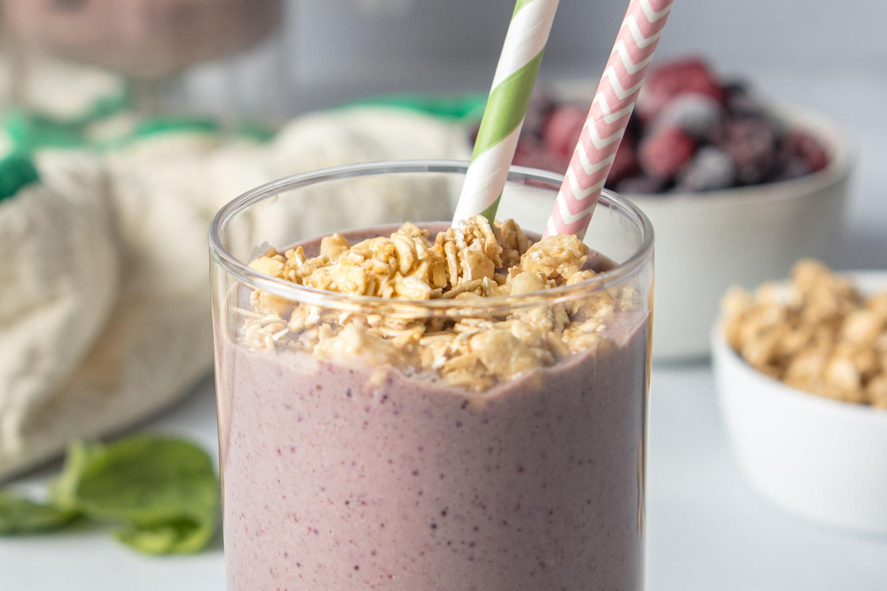 hand holding smoothie in a glass with granola on top