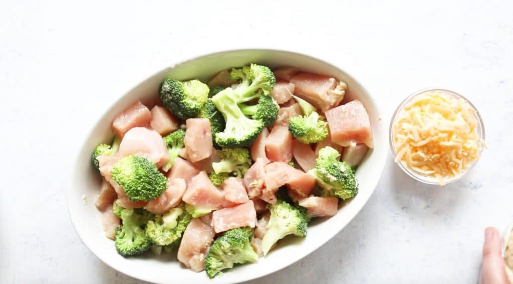 raw cubed chicken and broccoli in a white oval baking dish