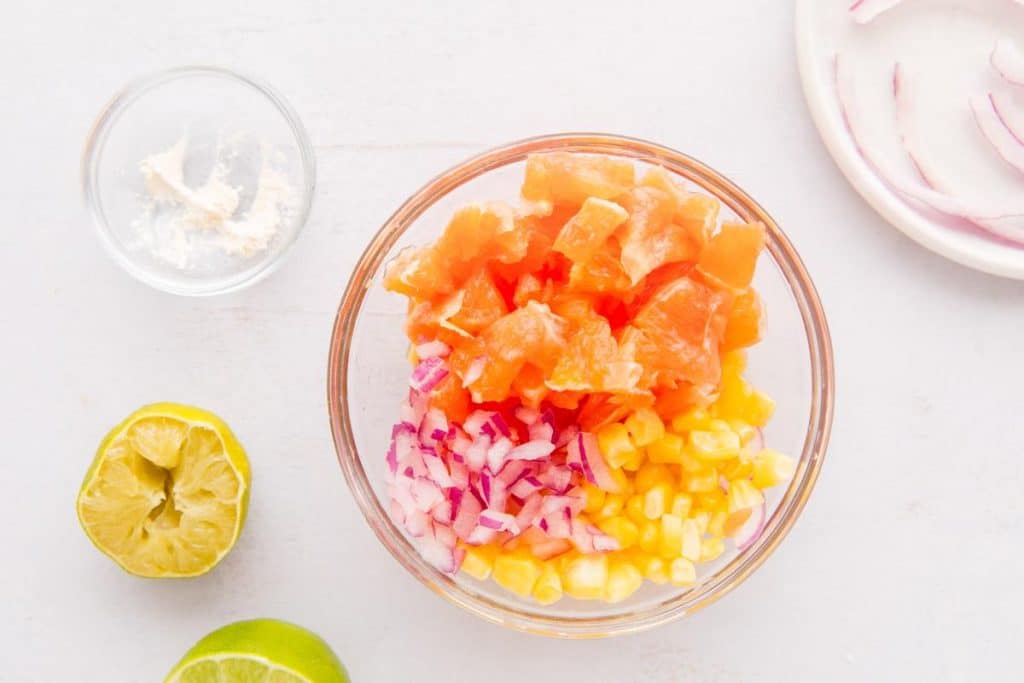 sliced oranges, corn, and red onion in a glass bowl