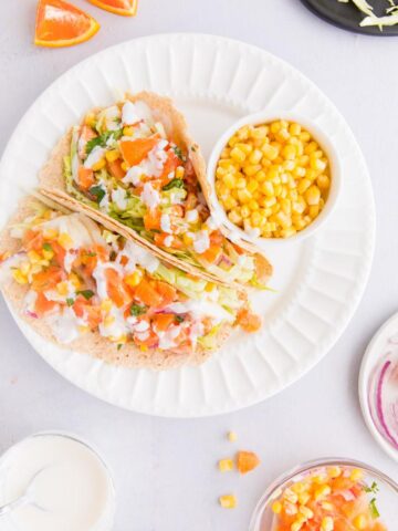 fish tacos with white sauce and orange salsa on a white plate