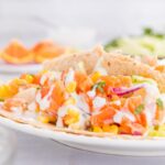 close up of fish tacos with white sauce and orange salsa on a plate