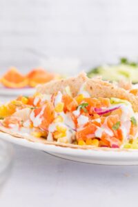 close up of fish tacos with white sauce and orange salsa on a plate