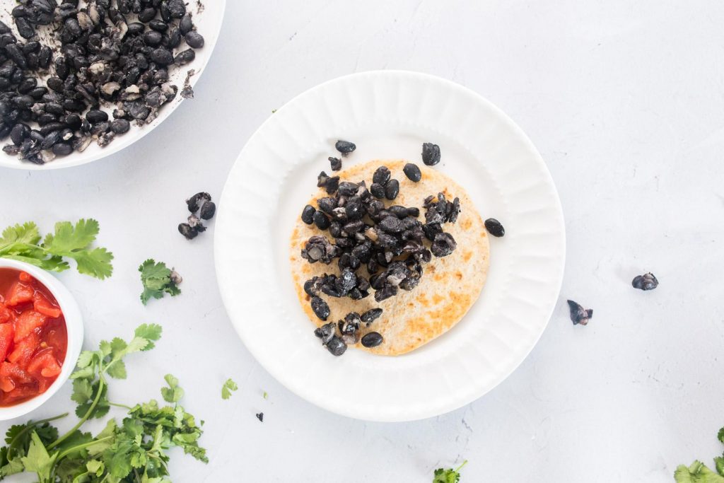 small tortilla with black beans on a white plate