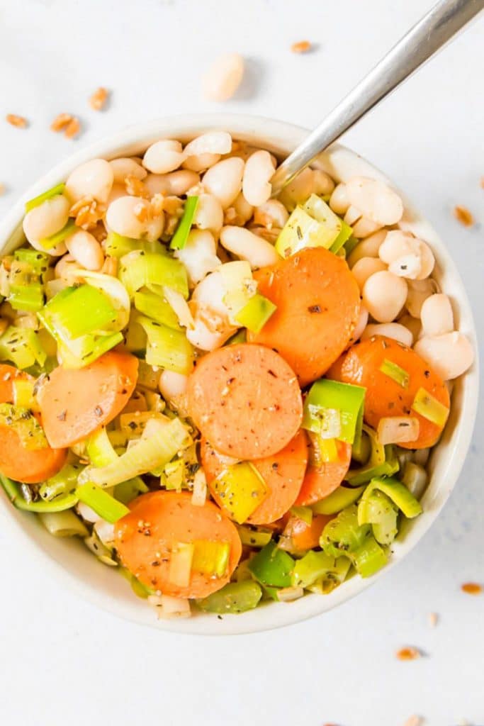 carrots, leeks, and white beans in a white bowl with a spoon in it
