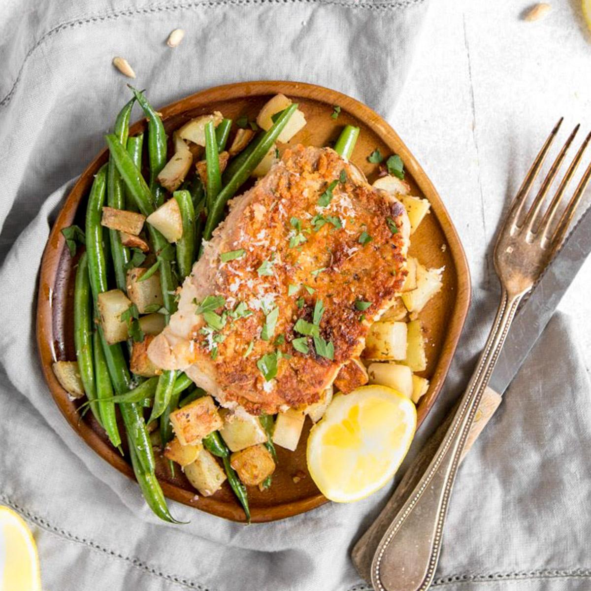 close up of pan seared pork chop, green beans, potatoes and a lemon on a plate