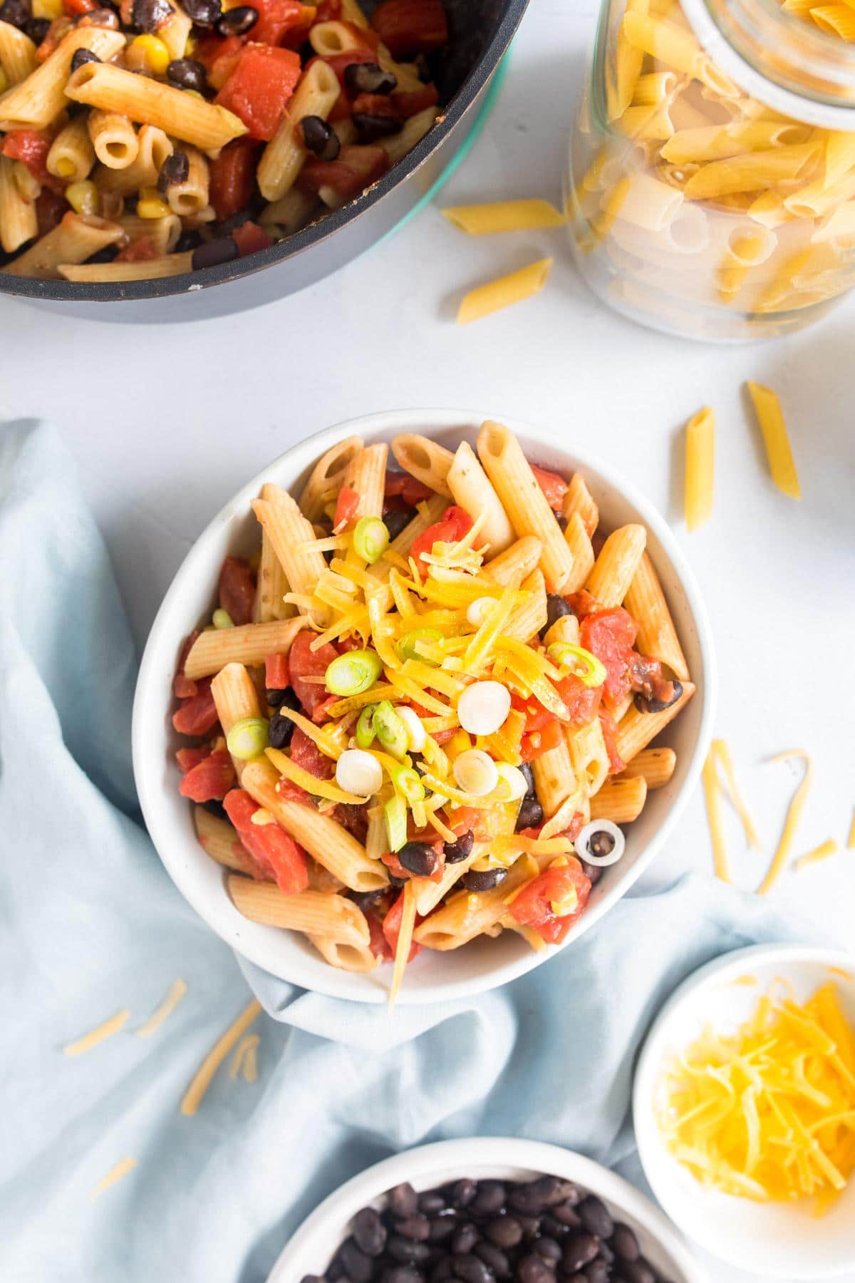 pasta with black beans and cheese on top in a white bowl with ingredients around.