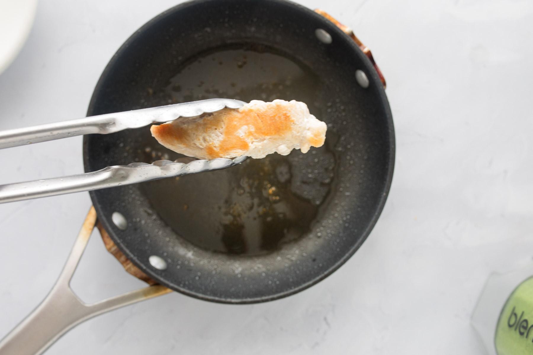 tongs holding a chicken tender over a frying pan