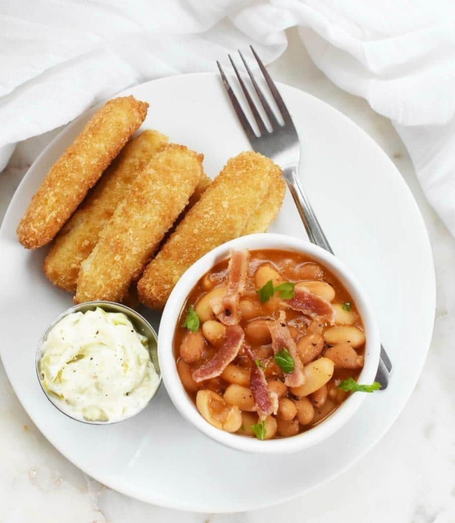 baked beans with bacon in a bowl with fish sticks on a plate