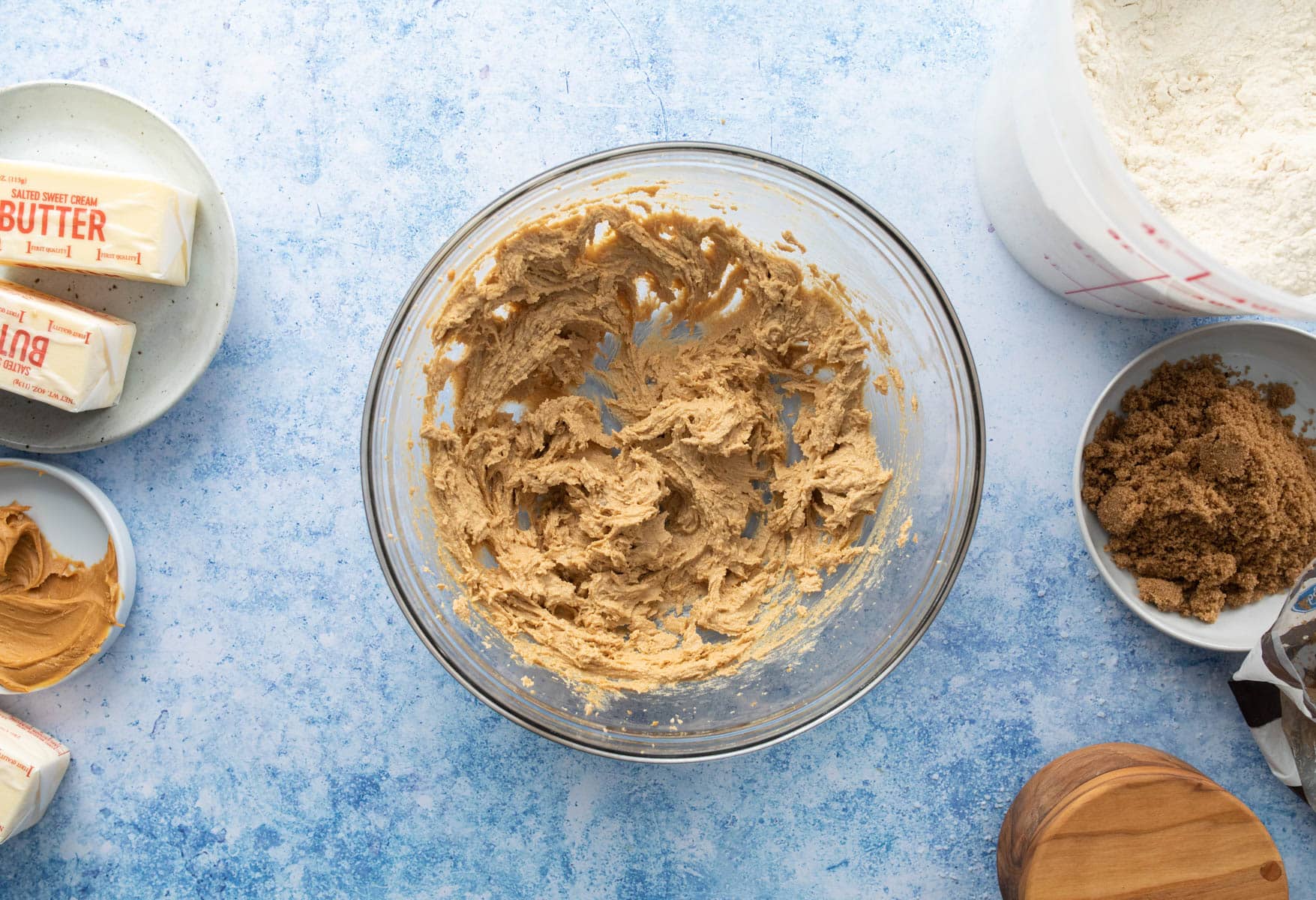 holding flours in a small bowl above wet ingredients for peanut butter cookies