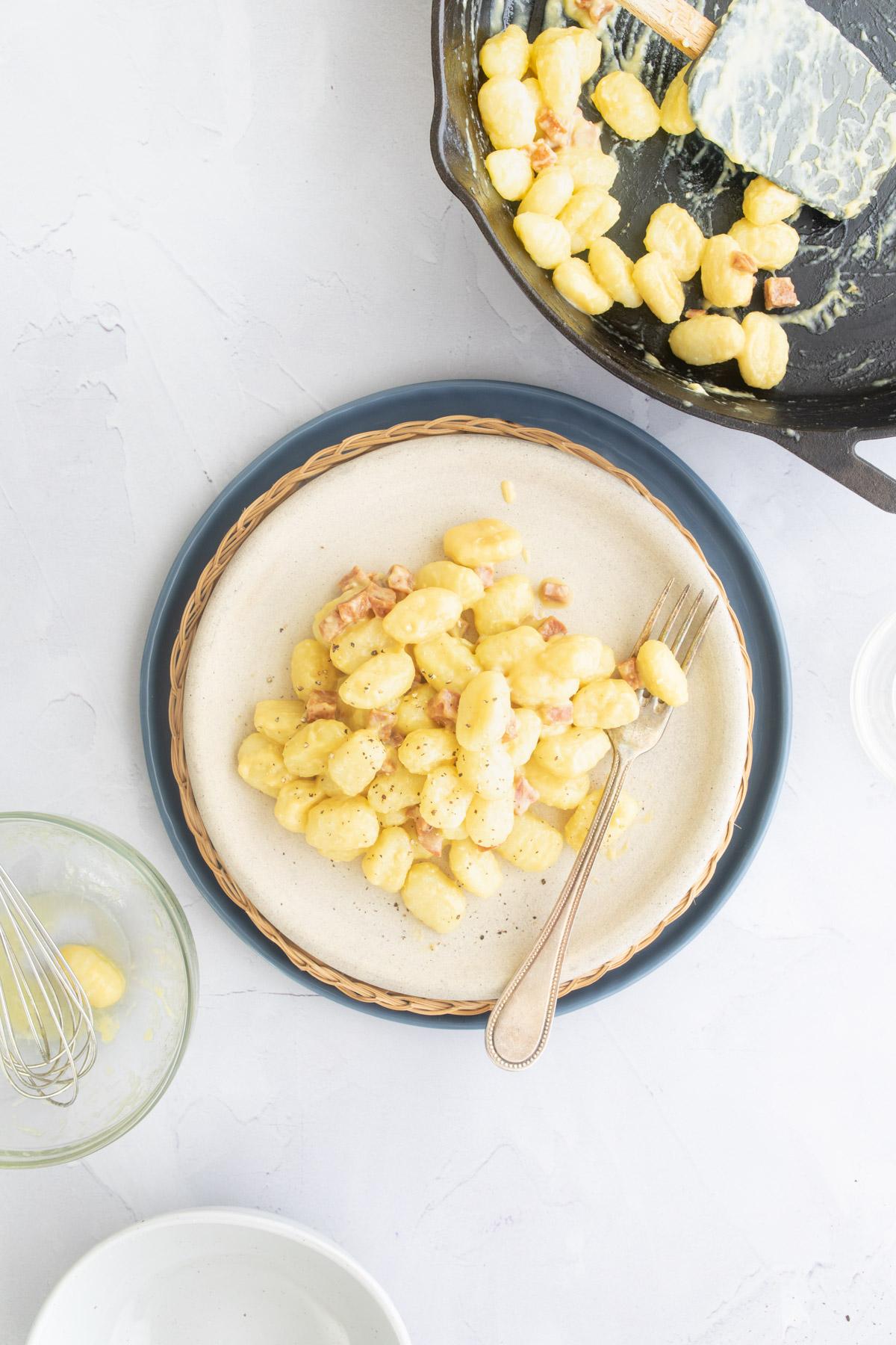 gnocchi carbonara on a plate next to skillet with gnocchi