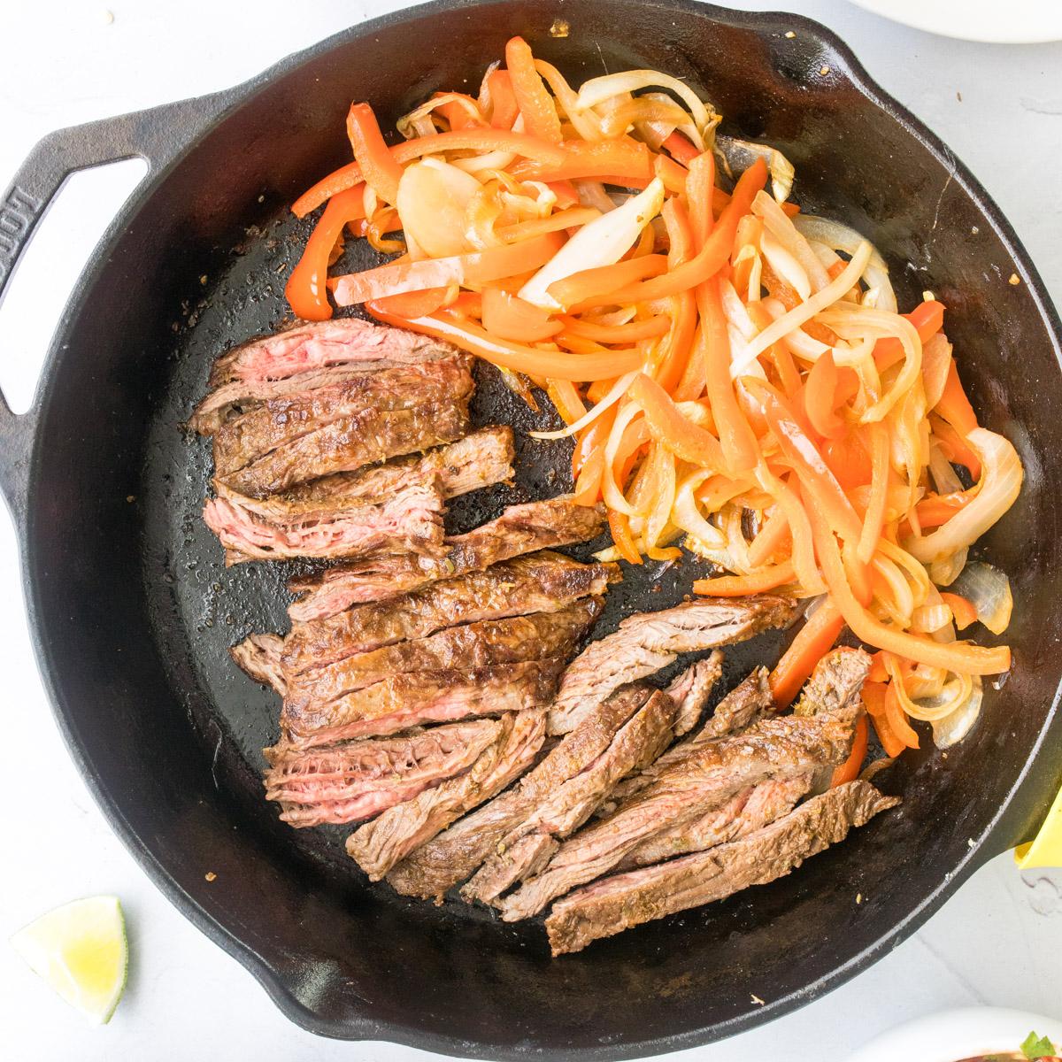 sliced steak, peppers and onions in a cast iron skillet